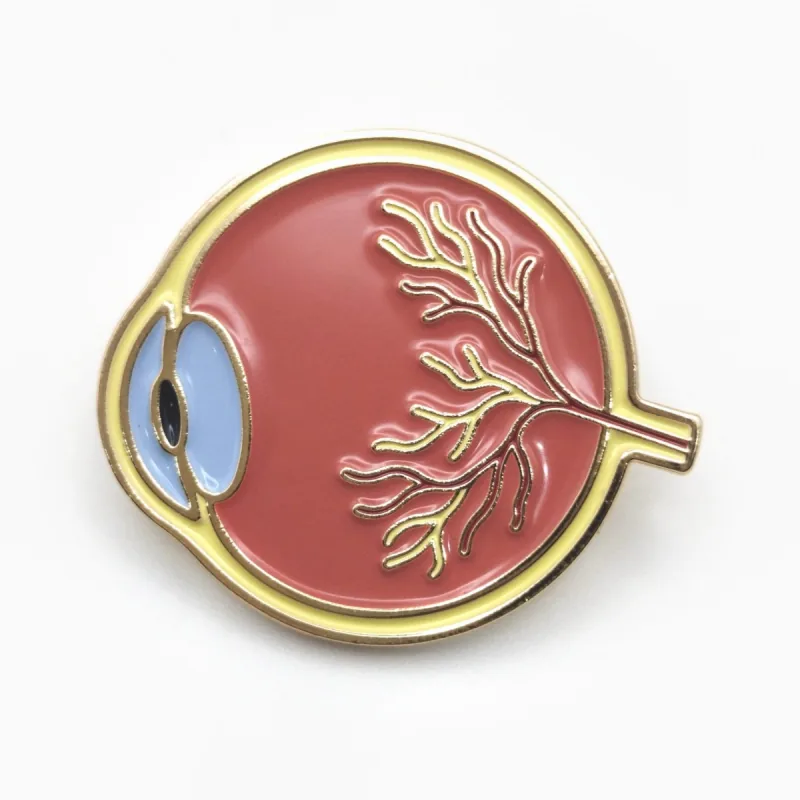 Pin redondo de esmalte suave con baño dorado que muestra un corte anatómico del ojo en coral, rojo y azul.