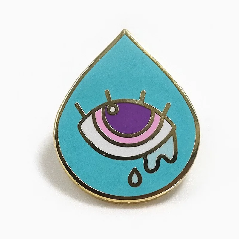 Pin de esmalte duro en forma de gota con baño dorado, que muestra un ojo morado con lágrimas sobre una gota turquesa.