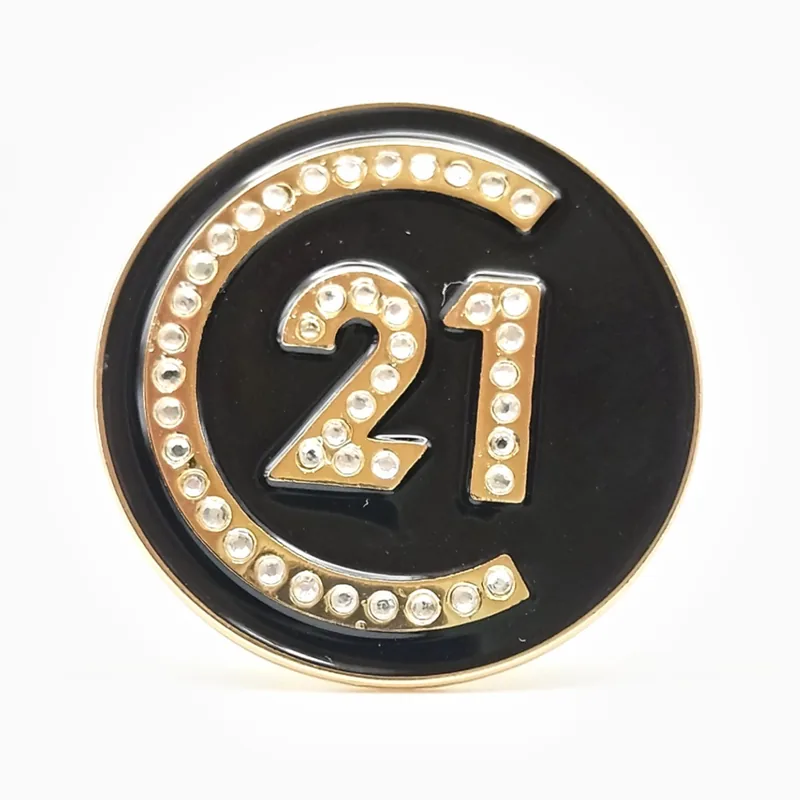 Pin redondo de esmalte negro y dorado con un aro de cristales alrededor del número 21, hecho para una empresa inmobiliaria.