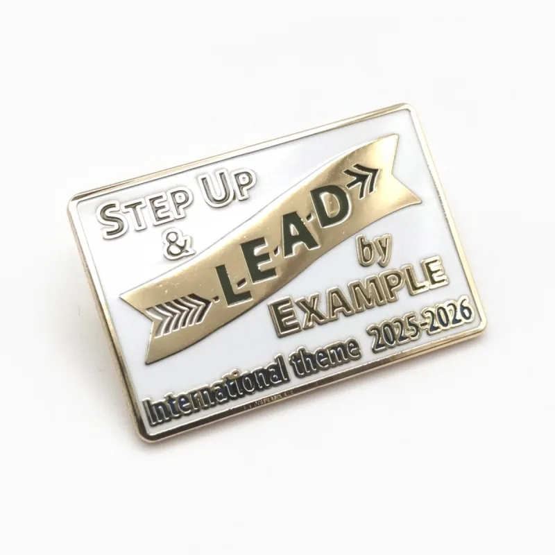 Pin rectangular de esmalte suave con baño dorado, fondo blanco y una banda dorada con el texto «Step Up & Lead by Example».