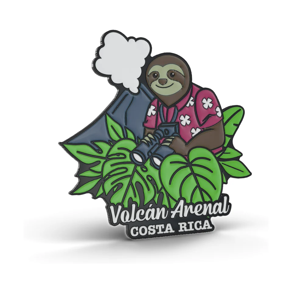 Imán de metal recortado con acabado epóxico: un perezoso con camisa floral rosada y binoculares entre hojas de costilla de Adán frente a un volcán humeante, con el texto Volcán Arenal Costa Rica.